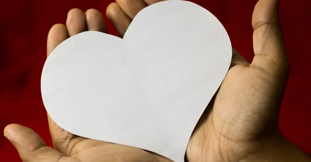 Close-up of two hands cradling a paper heart