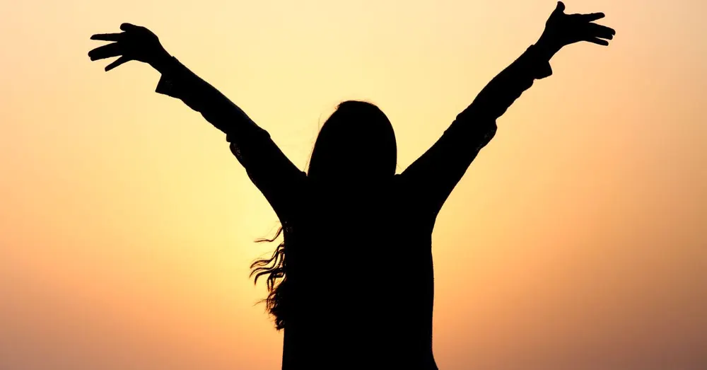 Silhouette of a woman with raised arms against a sunset sky