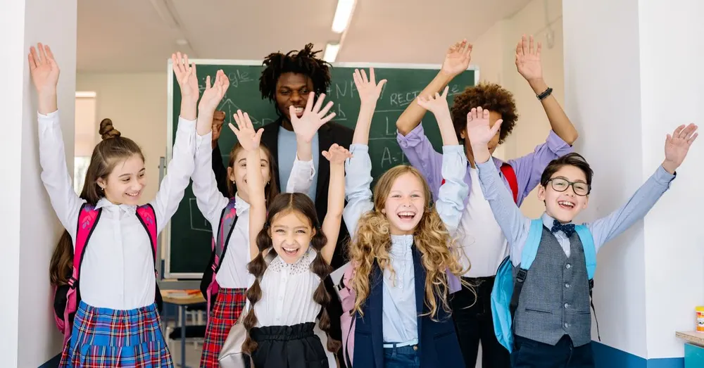 Group of diverse school children smiling with their hands raised